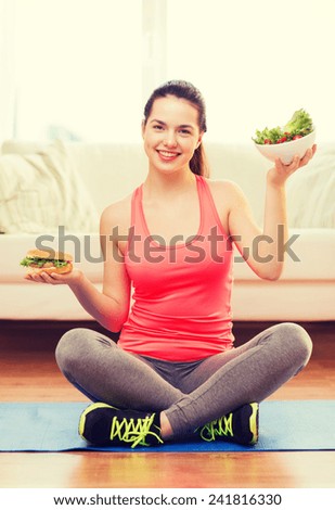 fitness, home and diet concept - smiling teenage girl with green salad and hamburger at home