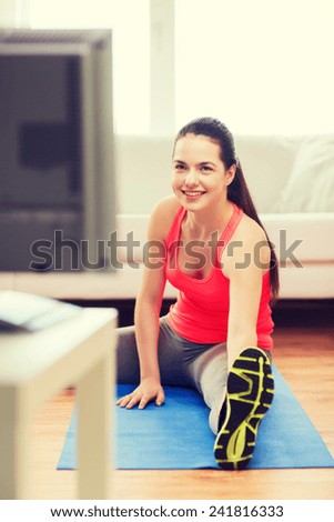 fitness, home and diet concept - smiling teenage girl streching on floor and watching tv at home