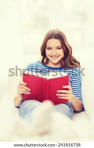 leasure and home concept - smiling teenage girl woman reading book and sitting on couch at home
