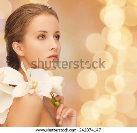 beauty, people and health concept - beautiful young woman with orchid flowers and bare shoulders over beige lights background