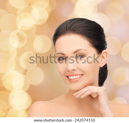 beauty, people and health concept - beautiful young woman touching her face over beige lights background