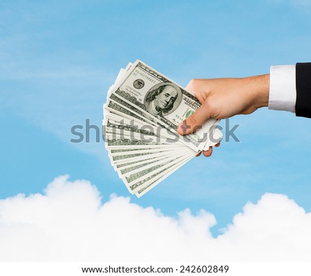 finances, people, savings and wealth concept - close up of male hand holding dollar cash money over blue sky and cloud background