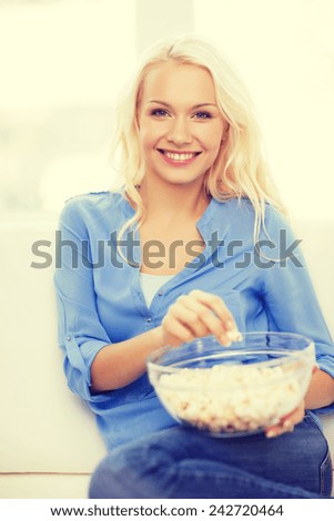 food, happiness and people concept - smiling young girl with popcorn ready to watch movie at home