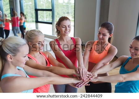 fitness, sport, friendship, teamwork and people concept - group of women with hands on top of each other in gym