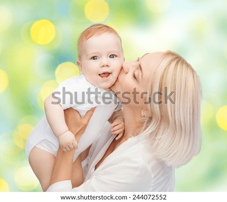 people, family, motherhood and children concept - happy mother hugging adorable baby over green lights background