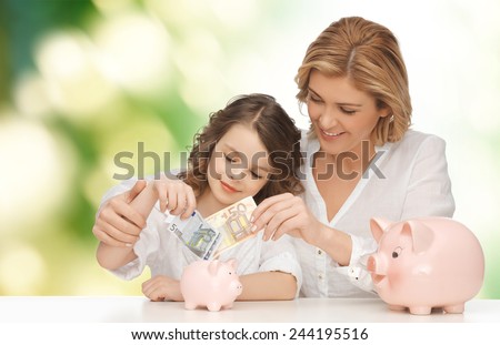 people, finances, family budget and savings concept - happy mother and daughter with piggy banks and paper money over green background