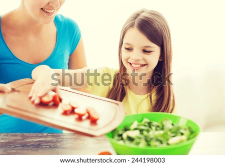 family, child, cooking and home concept - smiling little girl with mother adding tomatoes to salad in the kitchen