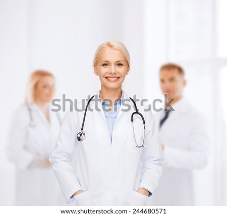 healthcare and medicine concept - smiling female doctor with stethoscope over background with group of medics in hospital