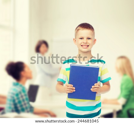 education, childhood, teamwork and school concept - smiling little student boy with blue book over group of students in classroom