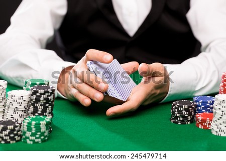 casino, gambling, poker, people and entertainment concept - close up of holdem dealer shuffling playing cards deck and chips on green table
