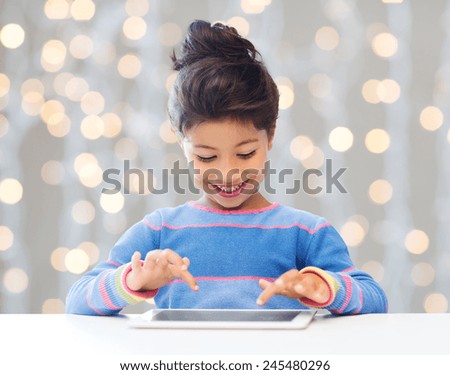 education, children, technology and people concept - happy little girl with tablet pc computer over holidays lights background