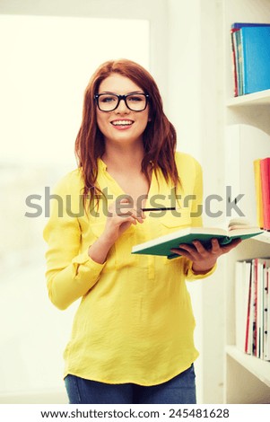 education concept - smiling redhead female student in eyeglasses with book and pencil in library
