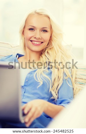 home, technology and internet concept - smiling woman sitting on the couch with laptop computer at home