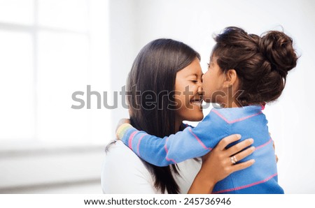 family, children and happy people concept - happy little girl hugging and kissing her mother over white room background