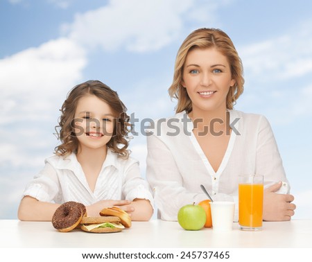 people, healthy lifestyle, family and food concept - happy mother and daughter eating healthy breakfast over blue sky background