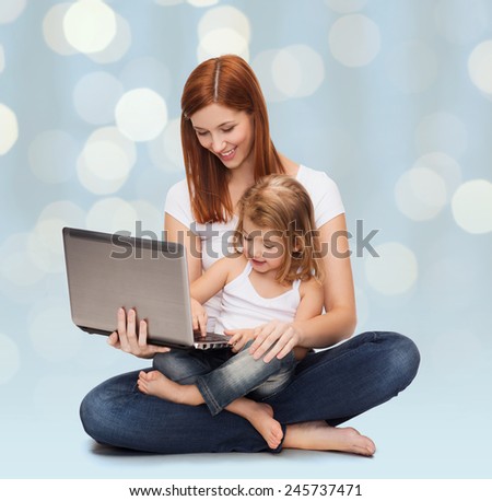 childhood, parenting and technology concept - happy mother with adorable little girl and laptop computer over holidays lights background