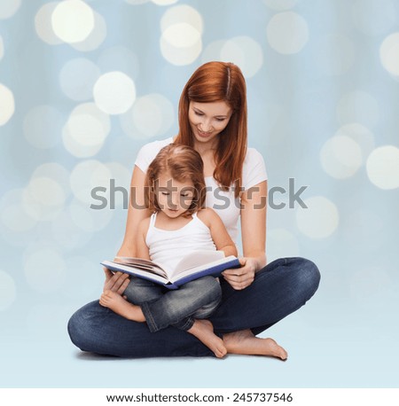 childhood, parenting and literature concept - happy mother with adorable little girl reading book over holidays lights background