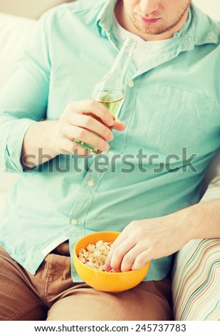 food, drinks, relax, leisure and people concept - close up of man with popcorn and beer sitting on couch at home