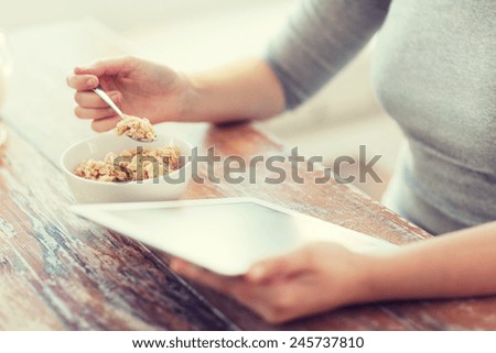 health, technology, internet, food and home concept - close up of woman eating porridge and using tablet pc computer