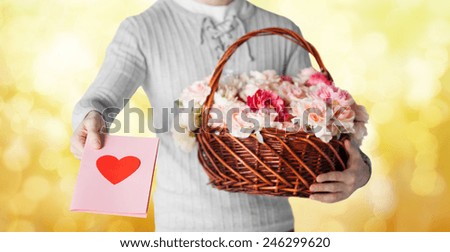holidays, people, feelings and greetings concept - close up of man holding basket full of flowers and giving postcard over yellow lights background