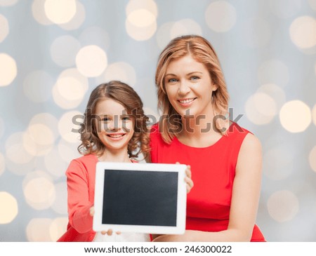 family, technology, people and christmas holidays concept - happy mother and daughter with tablet pc computer over lights background