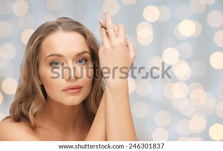 people, beauty, body and skin care concept - beautiful woman face and hands over holidays lights background