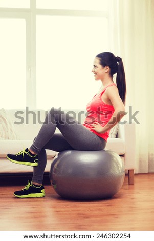 fitness, home and diet concept - smiling girl exercising with fitness ball at home
