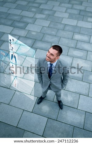 business, technology, mass media and people concept - young smiling businessman reading information from virtual screen outdoors