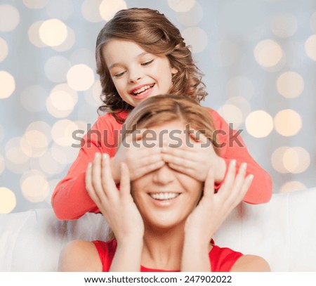 people, happiness, leisure, family and motherhood concept - happy mother and daughter playing guess who game over holidays lights background