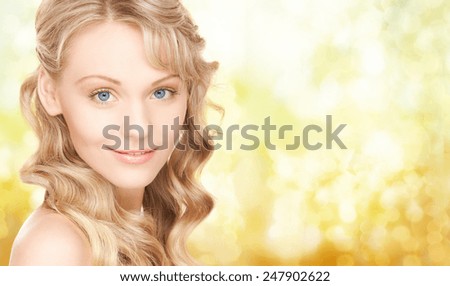 people, beauty, body and skin care concept - beautiful woman face and hands over yellow lights background
