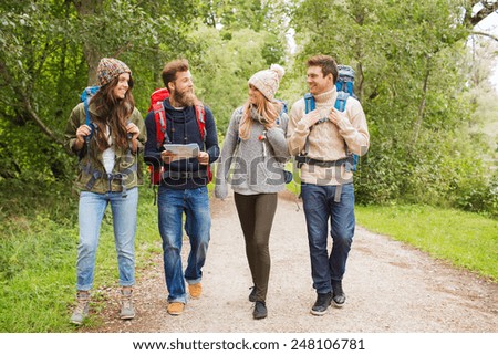 adventure, travel, tourism, hike and people concept - group of smiling friends with backpacks and map walking outdoors