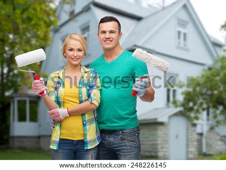 repair, people, real estate, home and family concept - smiling couple with paint rollers over house background