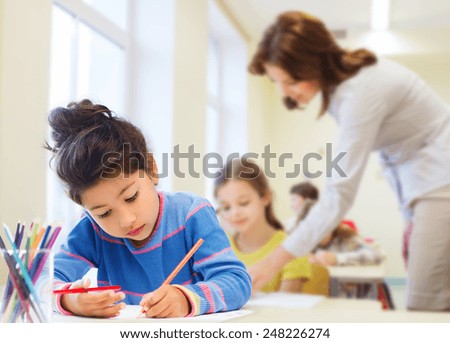 education, elementary school, children, creativity and people concept - happy little girl drawing with coloring pencils over classroom and teacher background