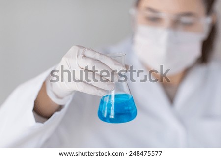 science, chemistry, biology, medicine and people concept - close up of young female scientist with flask making test or research in clinical laboratory
