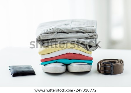 clothes and personal staff concept - close up of folded shirts, pants, belt, wallet and shoes on table at home