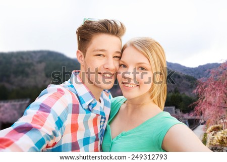 travel, tourism, technology, people and love concept - smiling couple with smartphone or camera taking selfie over asian village landscape background