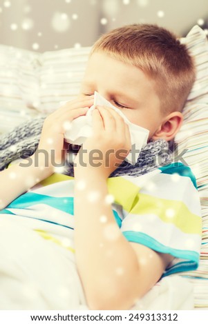 childhood, healthcare and people concept - ill boy with flu blowing nose into tissue at home