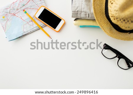 travel, summer vacation, tourism and objects concept - close up of folded clothes, smartphone and touristic map on table