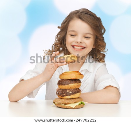 junk food, unhealthy eating, children and people concept happy smiling girl eating buns, donuts and burger over blue lights background