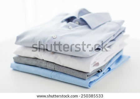 ironing, laundry, clothes, housekeeping and objects concept - close up of ironed and folded shirts on table at home