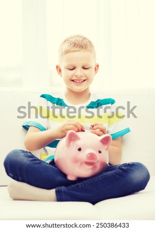 home, money, finances, childhood and people concept - smiling little boy with piggy bank sitting on coach at home