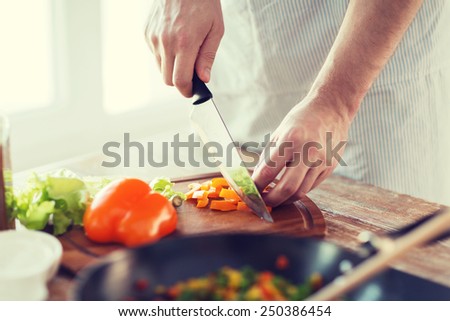 cooking, food and home concept - close up of male hand cutting pepper on cutting board at home
