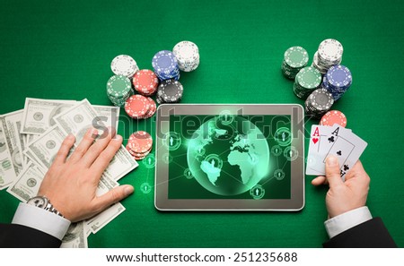 casino, online gambling, technology and people concept - close up of poker player holding playing cards, chips and earth projection with users icons on tablet pc computer screen at green casino table