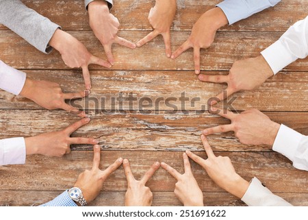 business, people, gesture and team work concept - close up of creative team showing victory hand sign on table in office