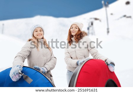 winter, leisure, sport, friendship and people concept - happy girl friends with snow tubes outdoors over mountain background