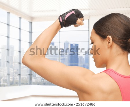 people, fitness, sport and bodybuilding concept - close up of sporty young woman flexing her biceps over gym or home background