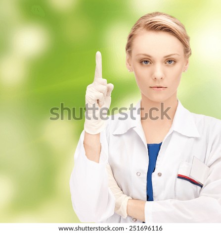 people, medicine and warning gesture concept - young female doctor pointing her finger up over green background