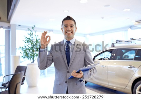 auto business, car sale, consumerism, gesture and people concept - happy man with clipboard showing thumbs up at auto show or salon