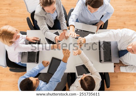 business, people, technology and team work concept - close up of creative team with laptop and tablet pc computers showing high five gesture and sitting at table in office