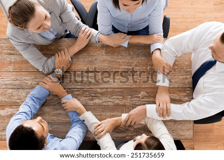 business, people, cooperation and team work concept - close up of creative team sitting at table and holding hands in office
